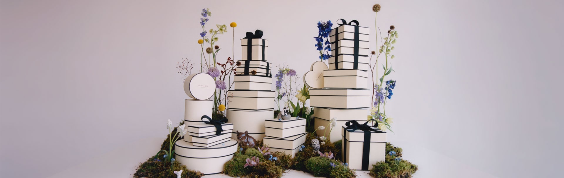 woman sitting on a hill, holding classic jo malone london black and cream gift boxes
