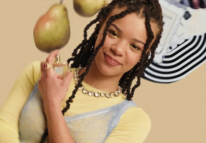 A person wearing yellow spins upside down, surrounded by a Jo Malone London display with fruit and black and white print. 