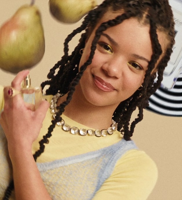 A person wearing yellow spins upside down, surrounded by a Jo Malone London display with fruit and black and white print. 